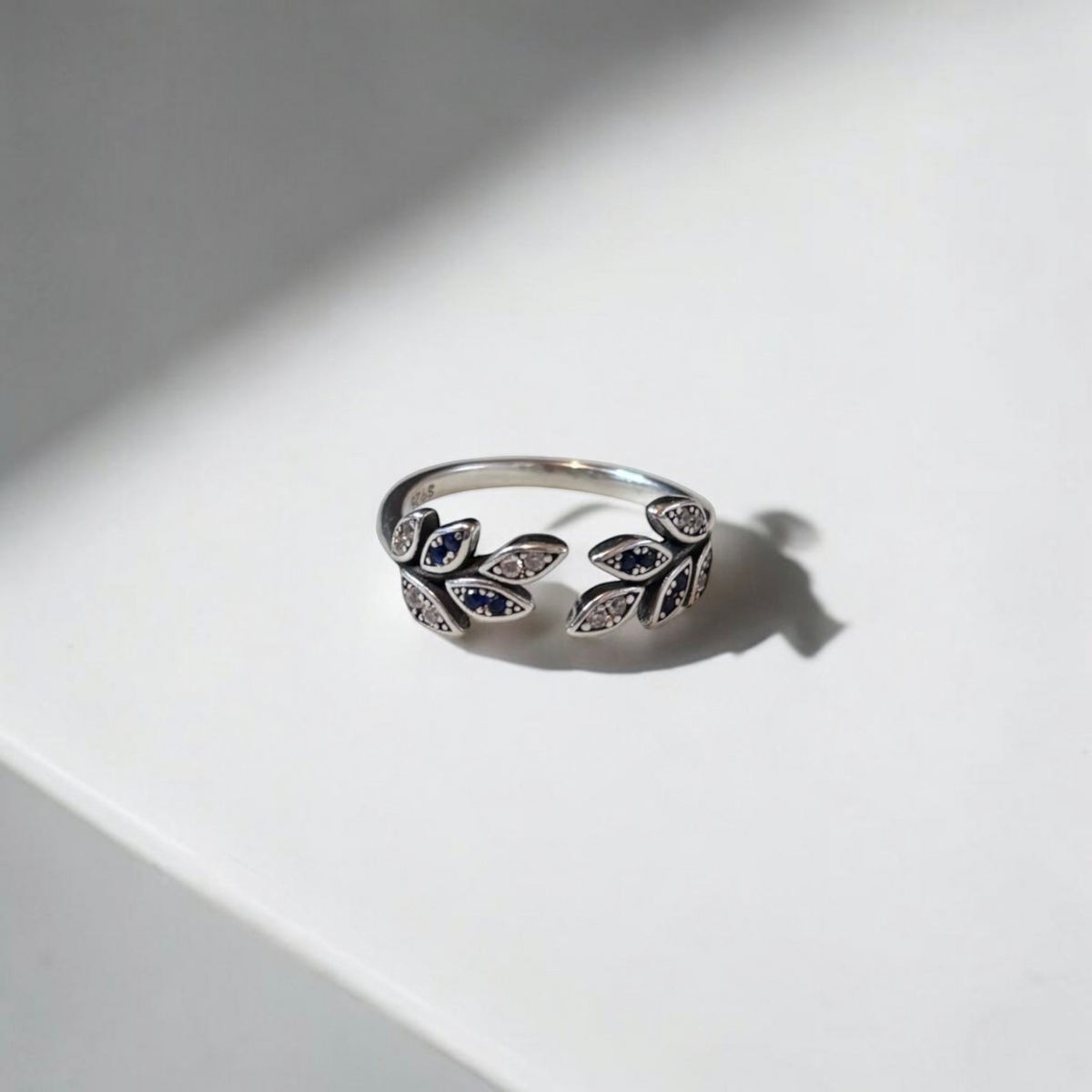 Omayra Boutique 925 sterling silver adjustable ring with a leaf design, blue and clear zircon stones on a white surface