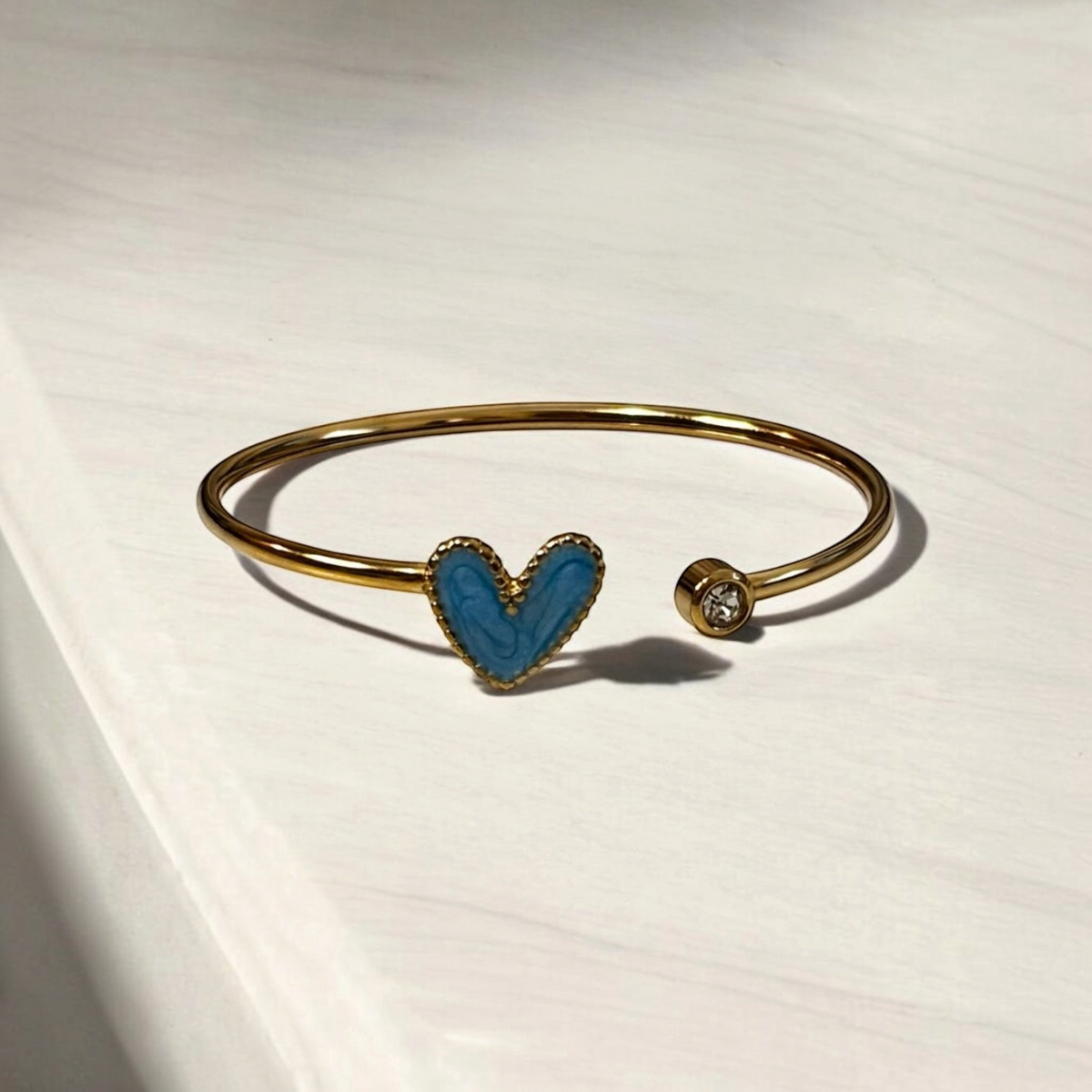 Omayra Boutique gold-tone stainless steel cuff bracelet with a blue heart charm and a small sparkling crystal accent.