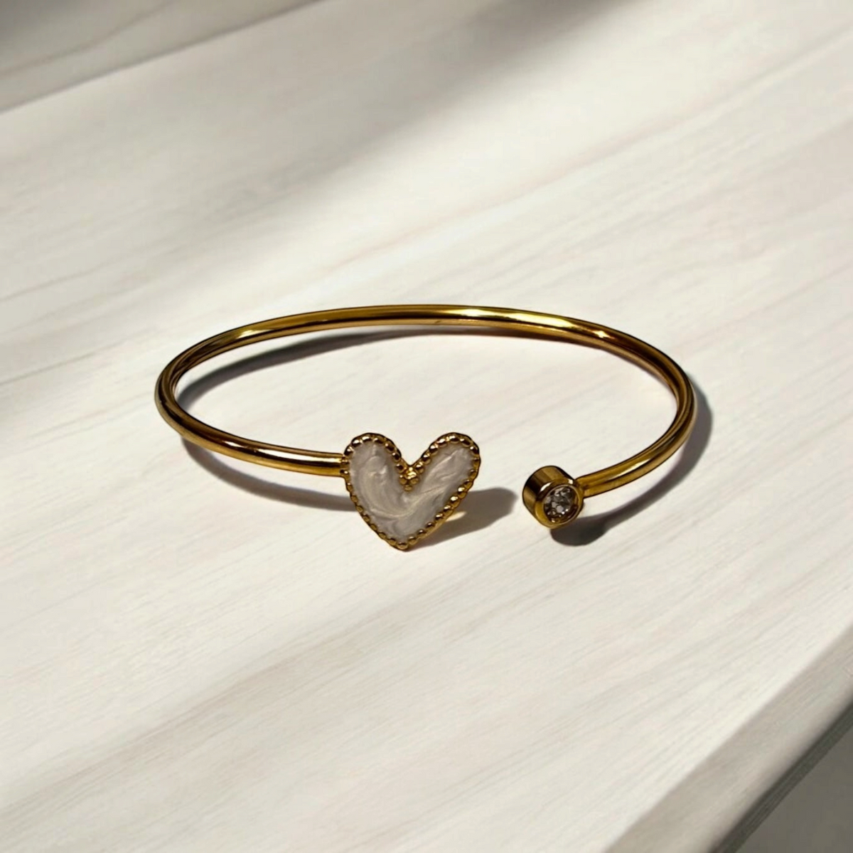 Omayra Boutique gold stainless steel cuff bracelet featuring a white marbled heart and a sparkling crystal accent.