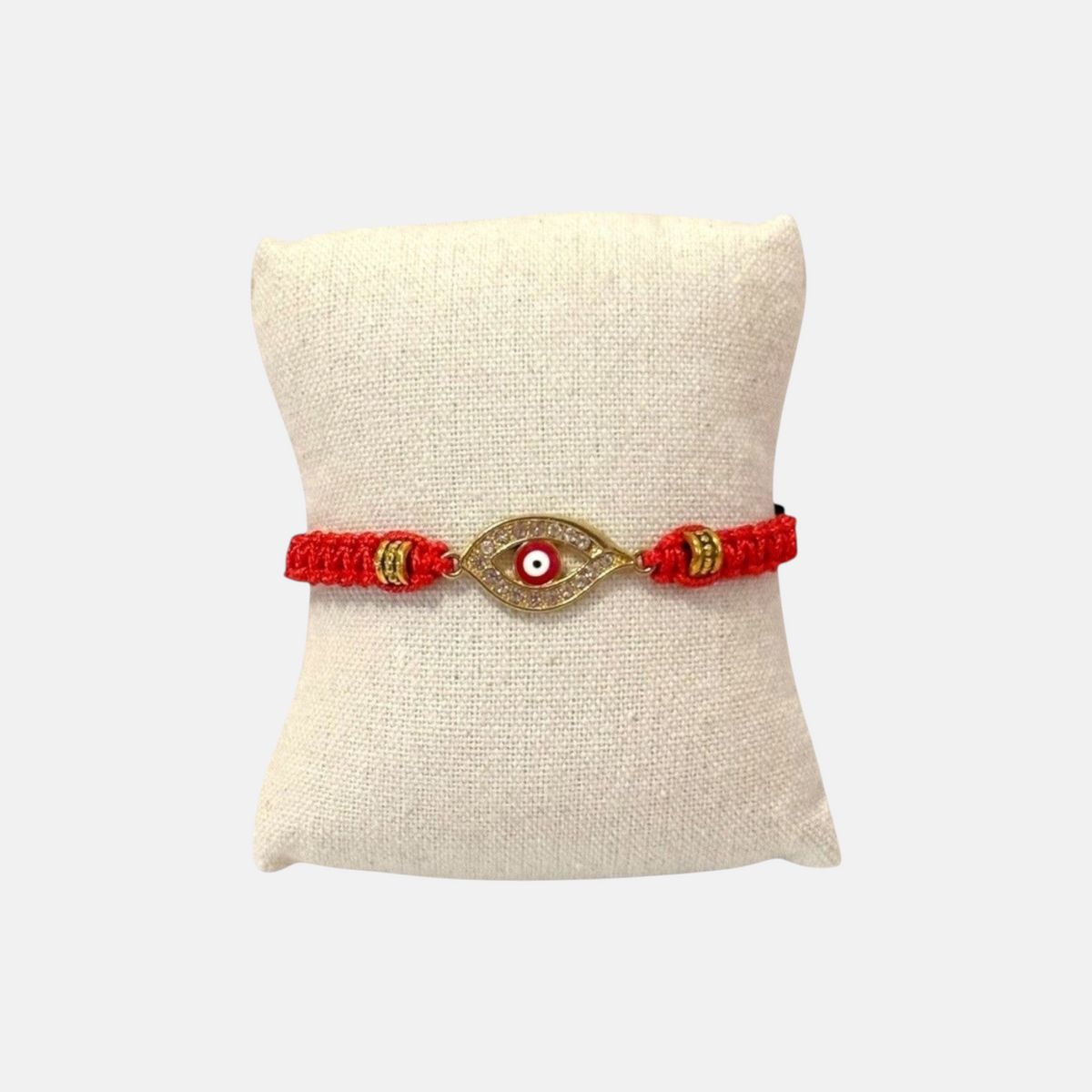 Omayra Boutique handmade red woven evil eye bracelet with gold-tone accents and adjustable cord on a display pillow
