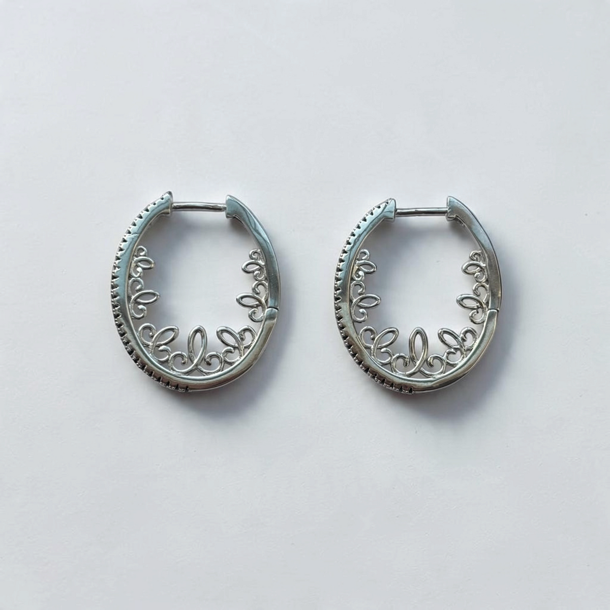 Omayra Boutique silver-tone oval hoop earrings featuring intricate scrollwork and black stone accents on a white background