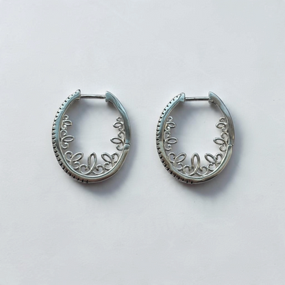 Omayra Boutique silver-tone oval hoop earrings featuring intricate scrollwork and black stone accents on a white background