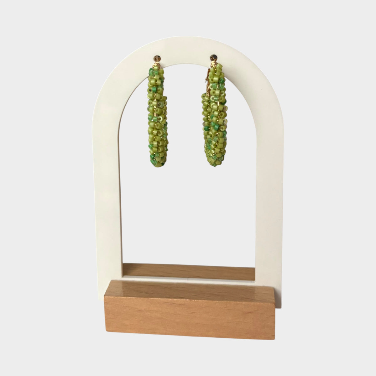 Omayra Boutique Lucky Green hoop earrings featuring vibrant beaded texture on a white arched display stand.