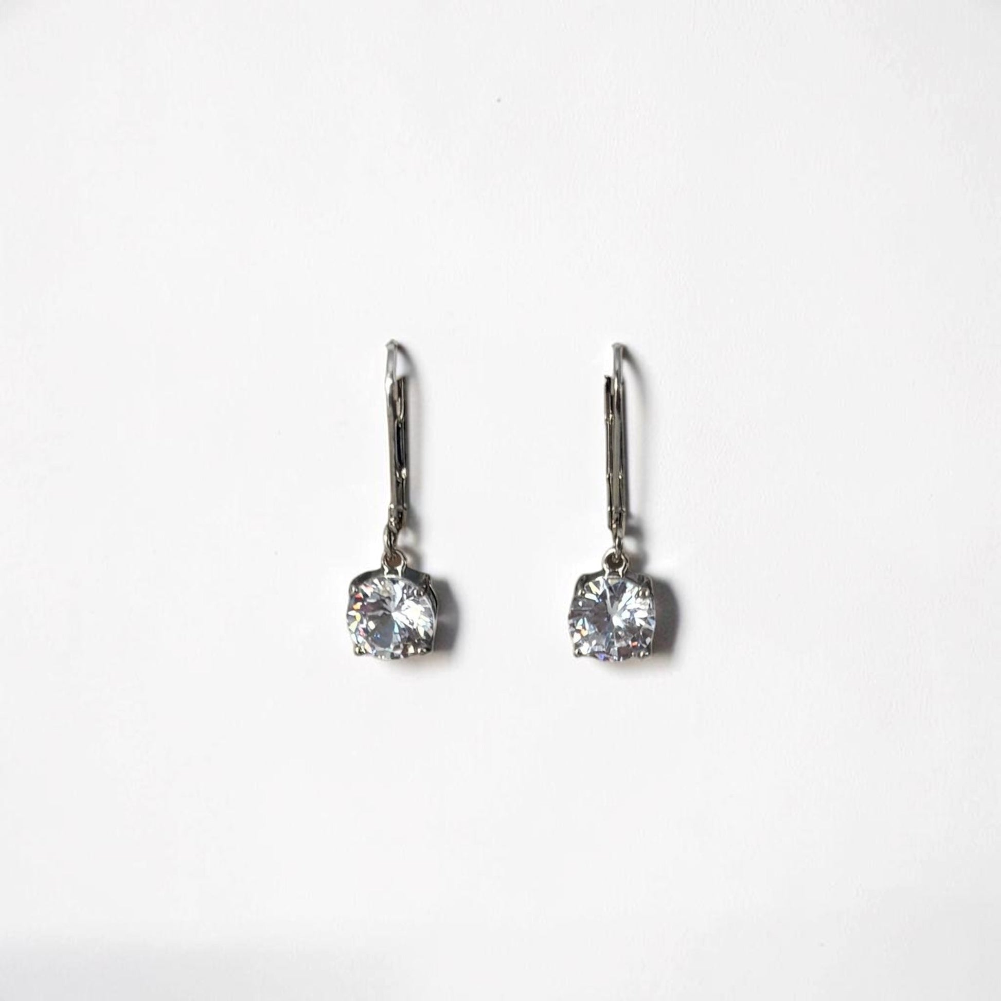 Omayra Boutique silver dangle earrings with sparkling cubic zirconia stones displayed on a white arch stand.