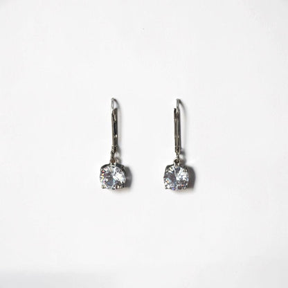 Omayra Boutique silver dangle earrings with sparkling cubic zirconia stones displayed on a white arch stand.